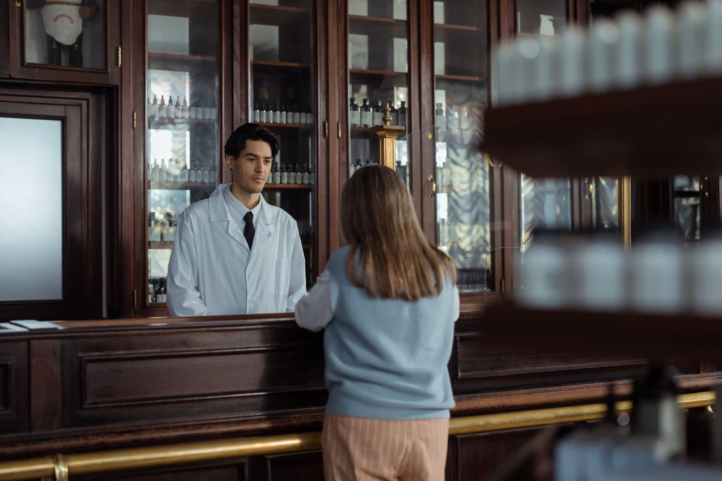 Apotheker berät eine Kundin am Holztresen einer Apotheke